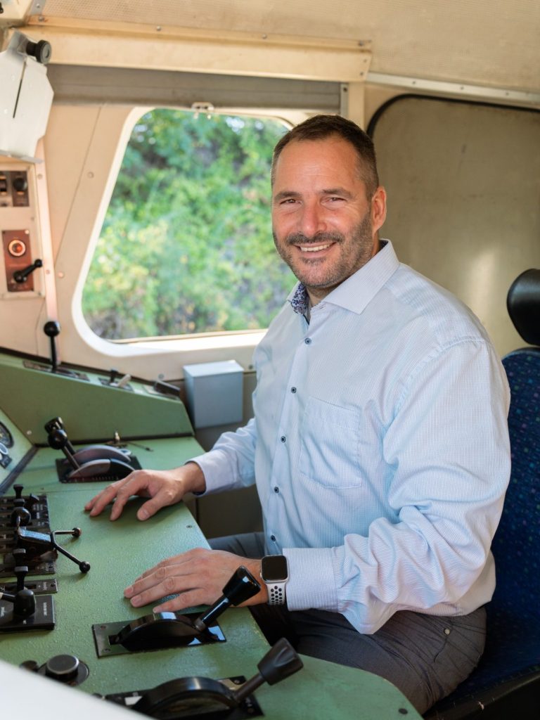 Jan Ristau sitzt lächelnd am Steuer eines Fahrzeugs in einem Führerstand einer Lokomotive.