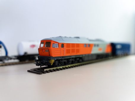 Modell einer orangefarbenen Lokomotive auf Schienen, mit Waggons im Hintergrund.