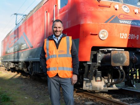 Jan Ristau in Warnweste steht neben einer roten Lokomotive auf einem Gleisbett.